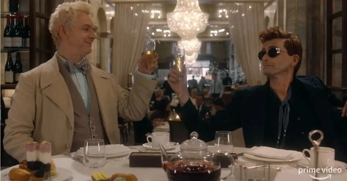 Blondwłosy Azirafal i rudy Crowley piją szampana przy stoliku w restauracji