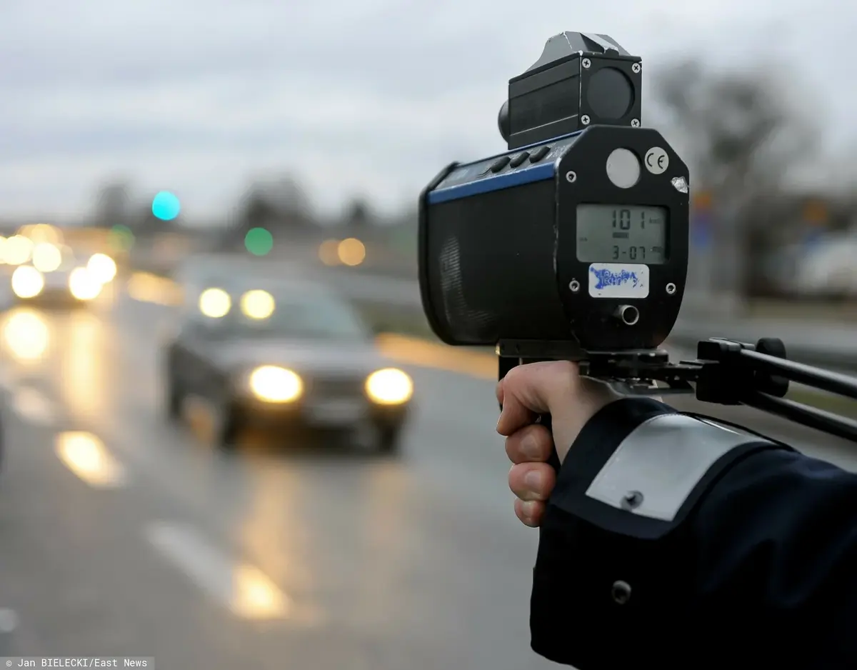 ręka trzymająca fotoradar wycelowany w stron jadących samochodów 