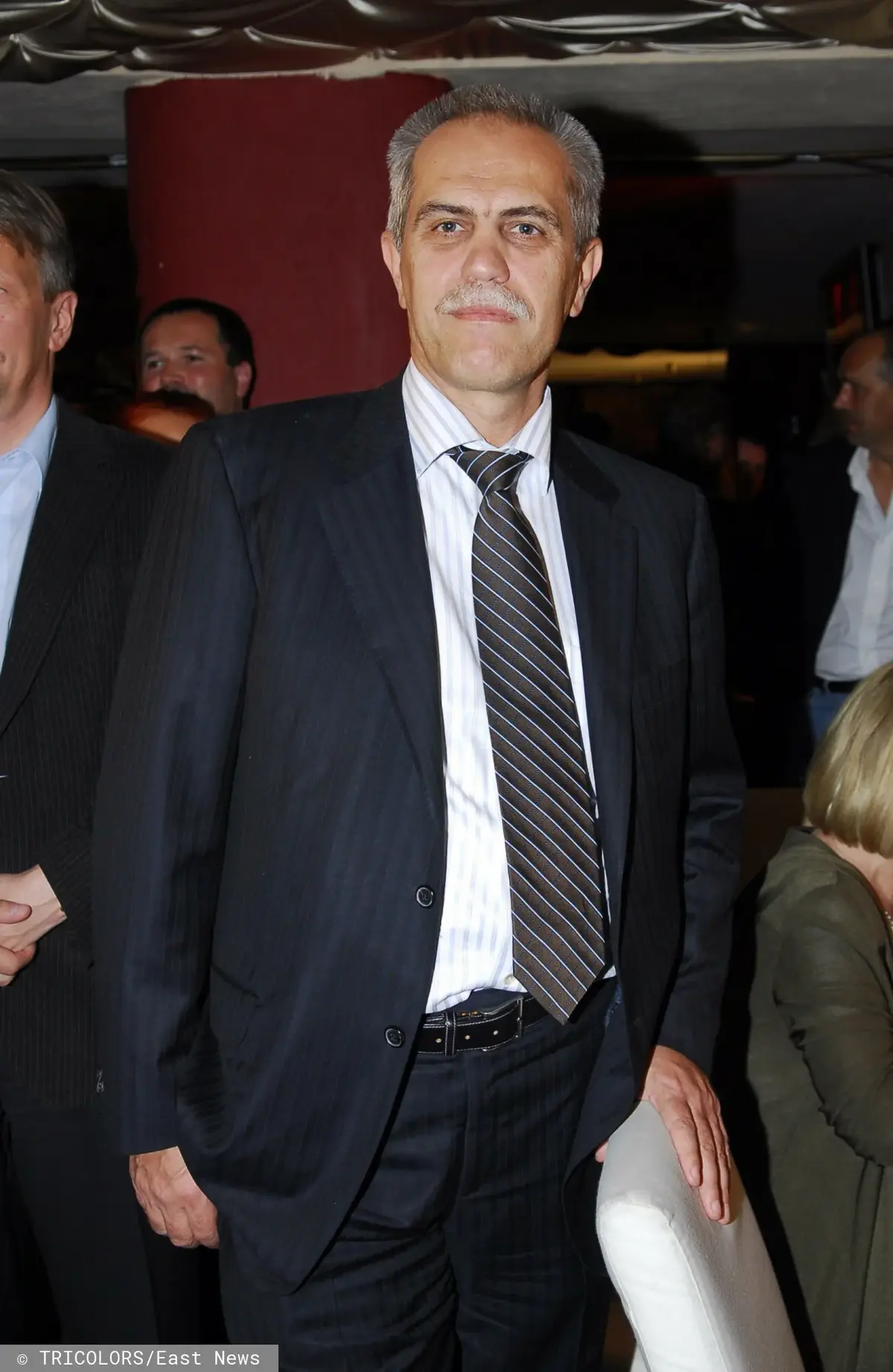 Zygmunt Solorz-Żak w czarnym garniturze, białej koszuli i ciemnym krawacie oparty o krzesło