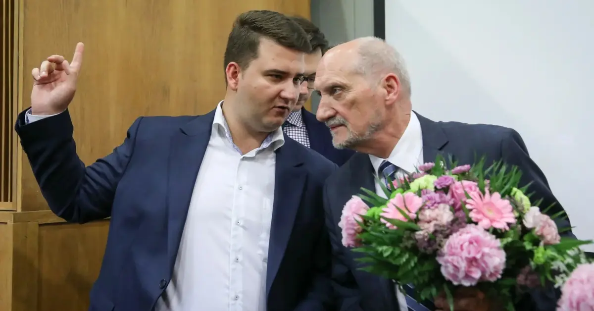 Bartłomiej Misiewicz pokazuje coś Antoniemu Macierewiczowi, który trzyma bukiet kwiatów 