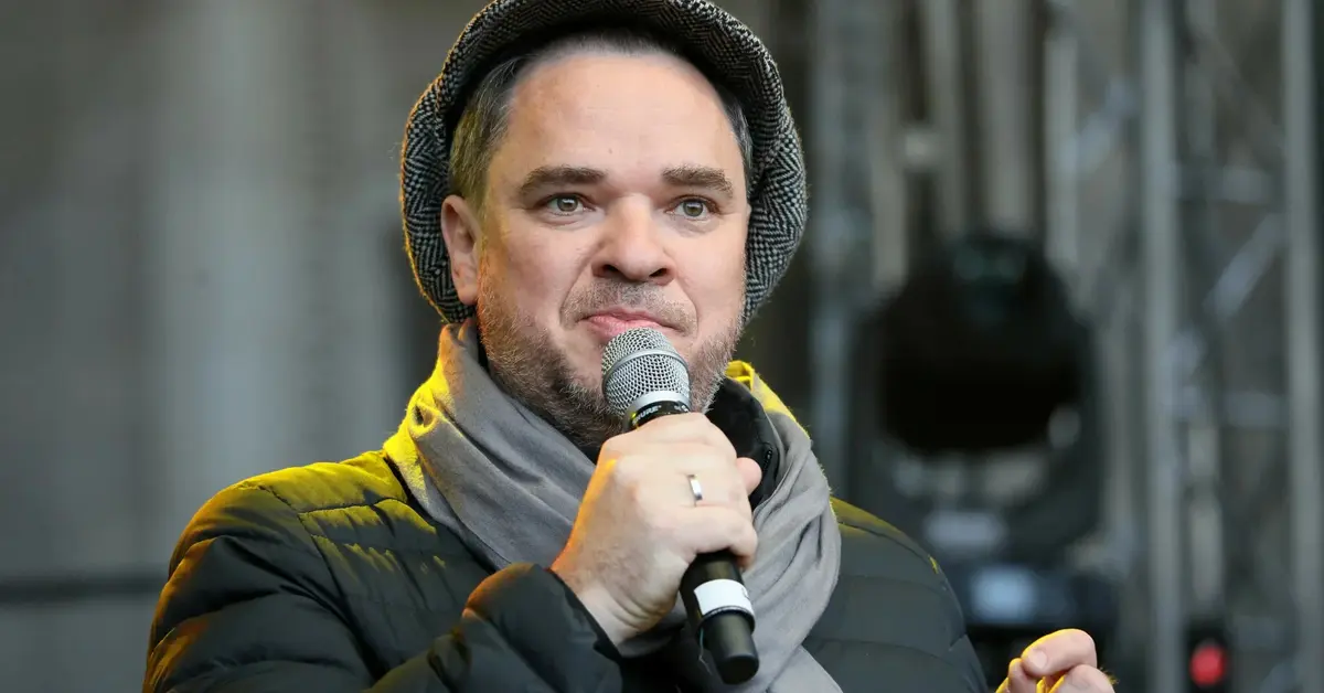 Grzegorz Kasdepke w czapce dzierży mikrofon.