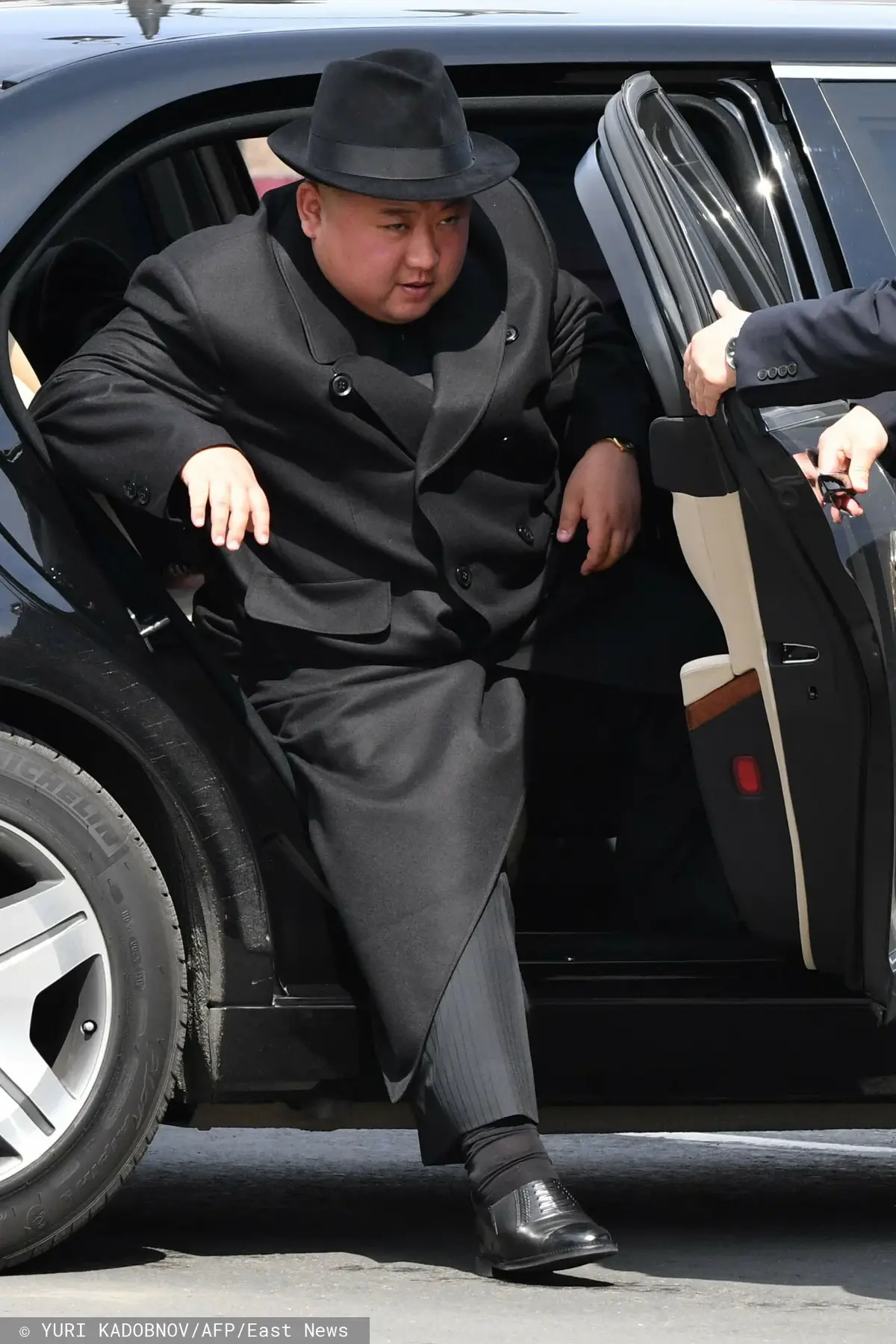 Kim Dzong Un w czarnym ubraniu i czarnym kapelusz wysiadający z czarnego samochodu