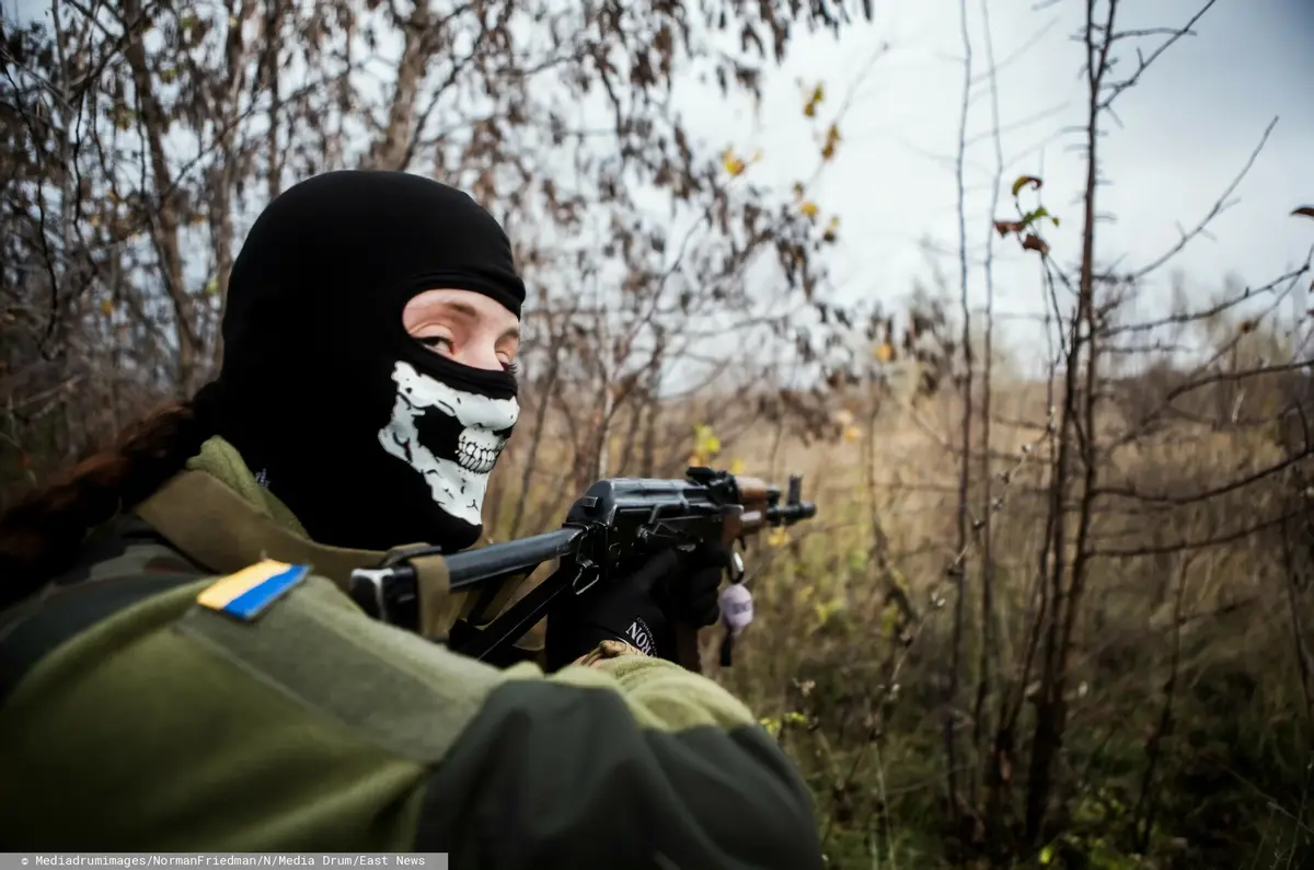 ukraiński żołnierz z maską z trupią czaszką na twarzy celuje z karabinu i patrzy w obiektyw