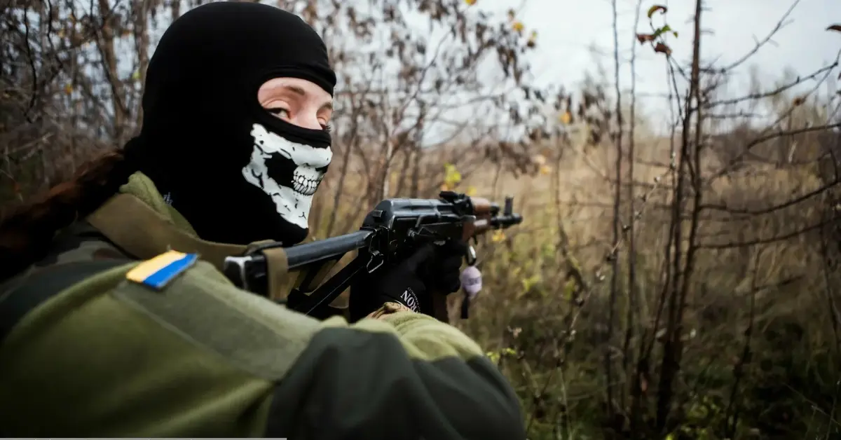 ukraiński żołnierz z maską z trupią czaszką na twarzy celuje z karabinu i patrzy w obiektyw