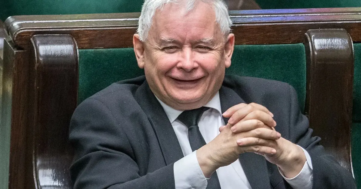 Uśmiechający się Jarosław Kaczyński ze złożonymi rękoma rozparty w swoim miejscu poselskim na sali plenarnej Sejmu 