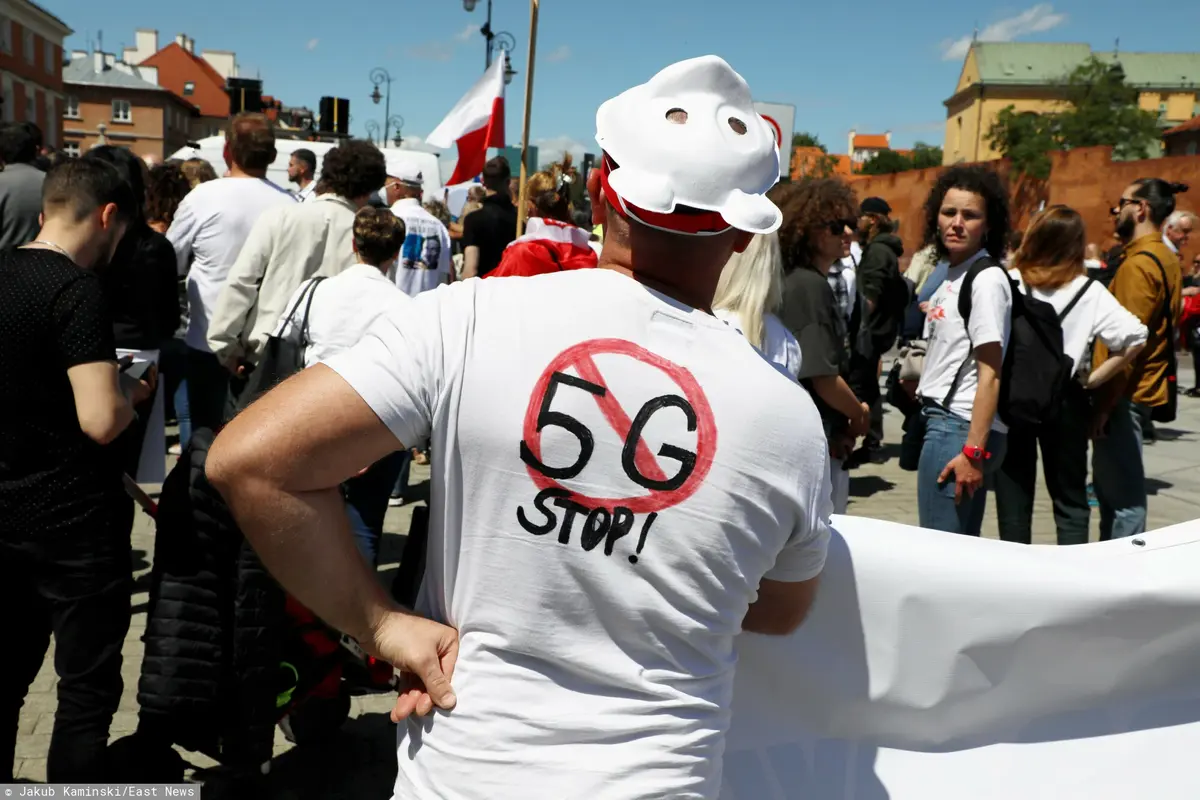 mężczyzna w białej koszulce z przekreślonym znakiem 5G stojący tyłem