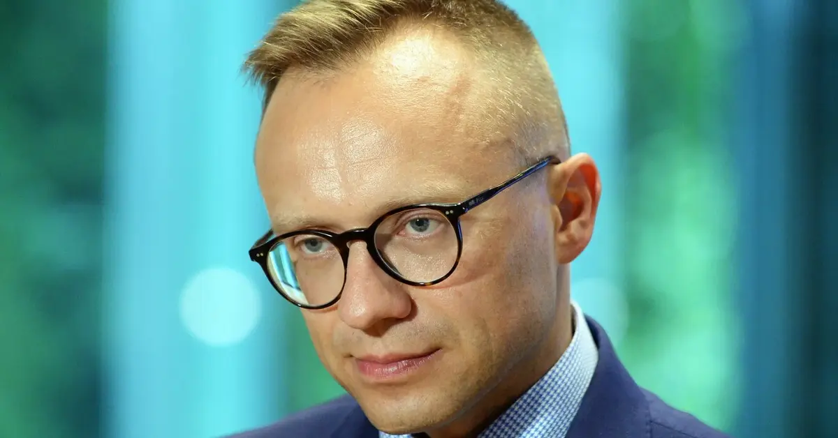 Artur Soboń w garniturze w okularach na zielonkawym tle