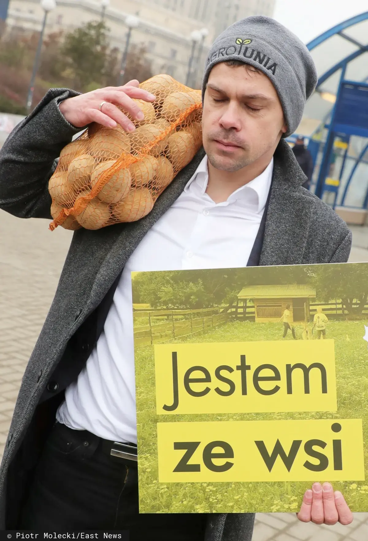 Michał Kołodziejczak z workiem ziemniaków i tablicą z napisem "Jestem ze wsi"