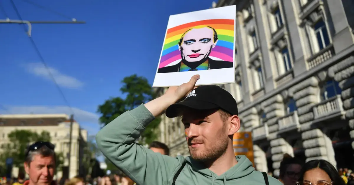 Protestujący trzyma podobiznę Władimira Putina na tle flagi LGBT.
