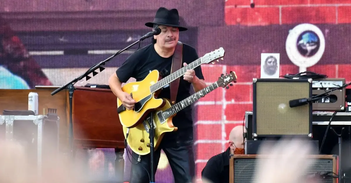 Carlos Santana trzyma dwie gitary i gra na jednej z nich.