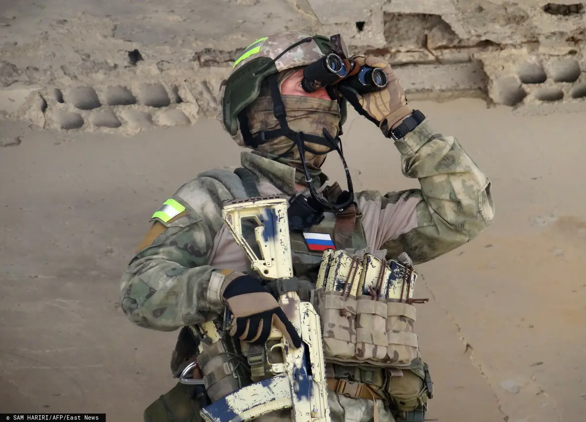 Rosyjski żołnierz w mundurze polowym patrzy w lornetkę z bronią w ręku
