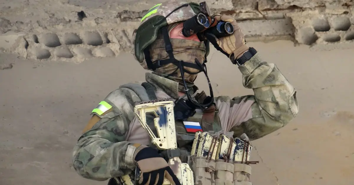 Rosyjski żołnierz w mundurze polowym patrzy w lornetkę z bronią w ręku