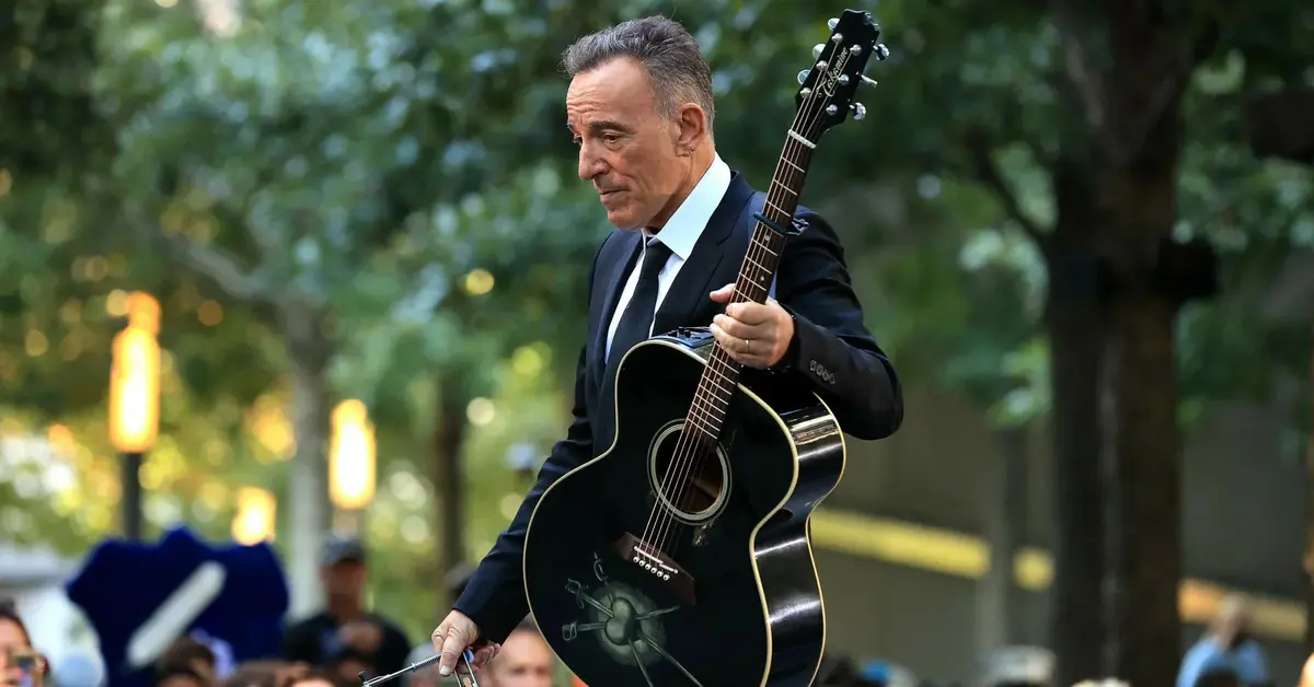 Bruce Springsteen w garniturze z czarną gitarą akustyczną.