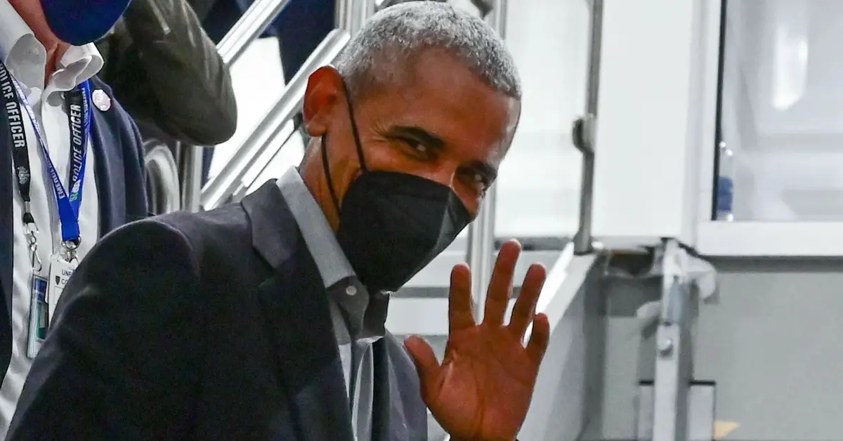 Barack Obama w maseczce macha ręką do kamery.