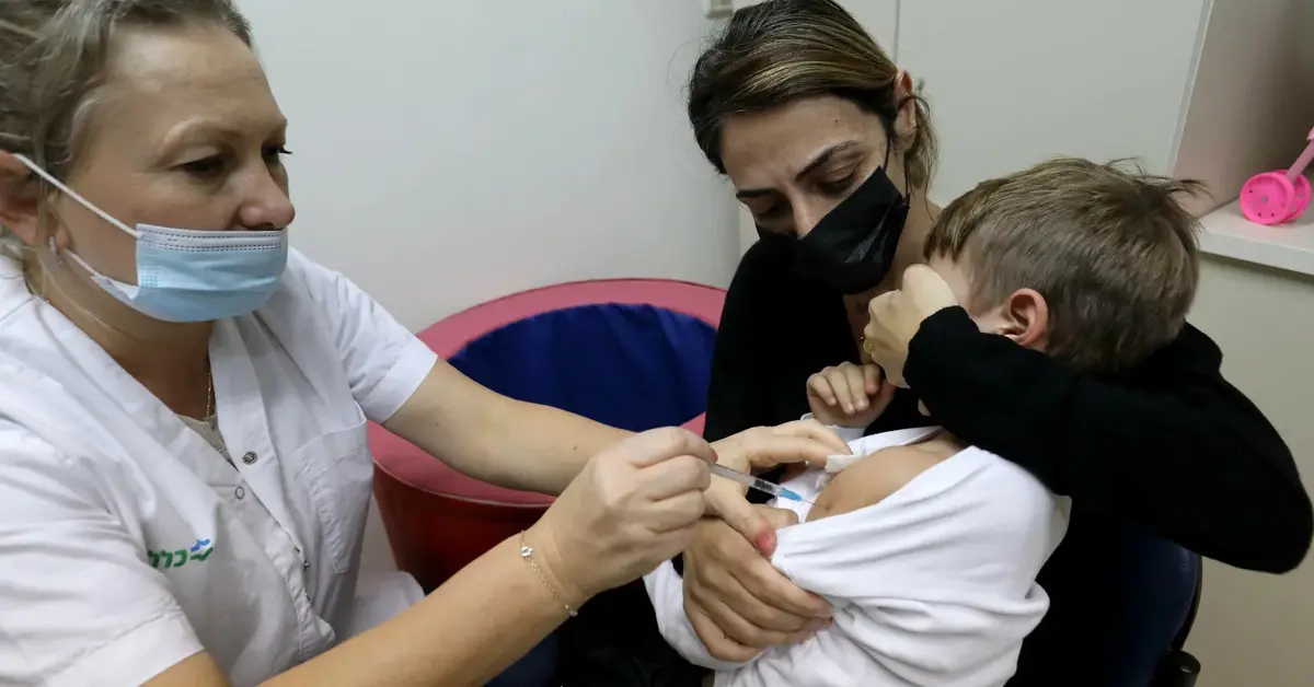 Pielęgniarka w maseczce robi zastrzyk przerażonemu chłopcu, którego trzyma matka, zasłaniając mu oczy