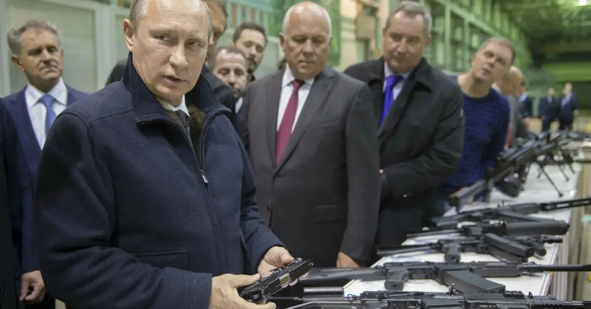 putin w czarnej kurtce, wraz z innymi ludźmi ogląda karabiny i pistolety ułożone na stole