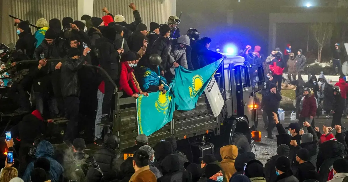 Tłum ludzi na ulicy i na ciężarówce na której są też dwie flagi Kazachstanu 