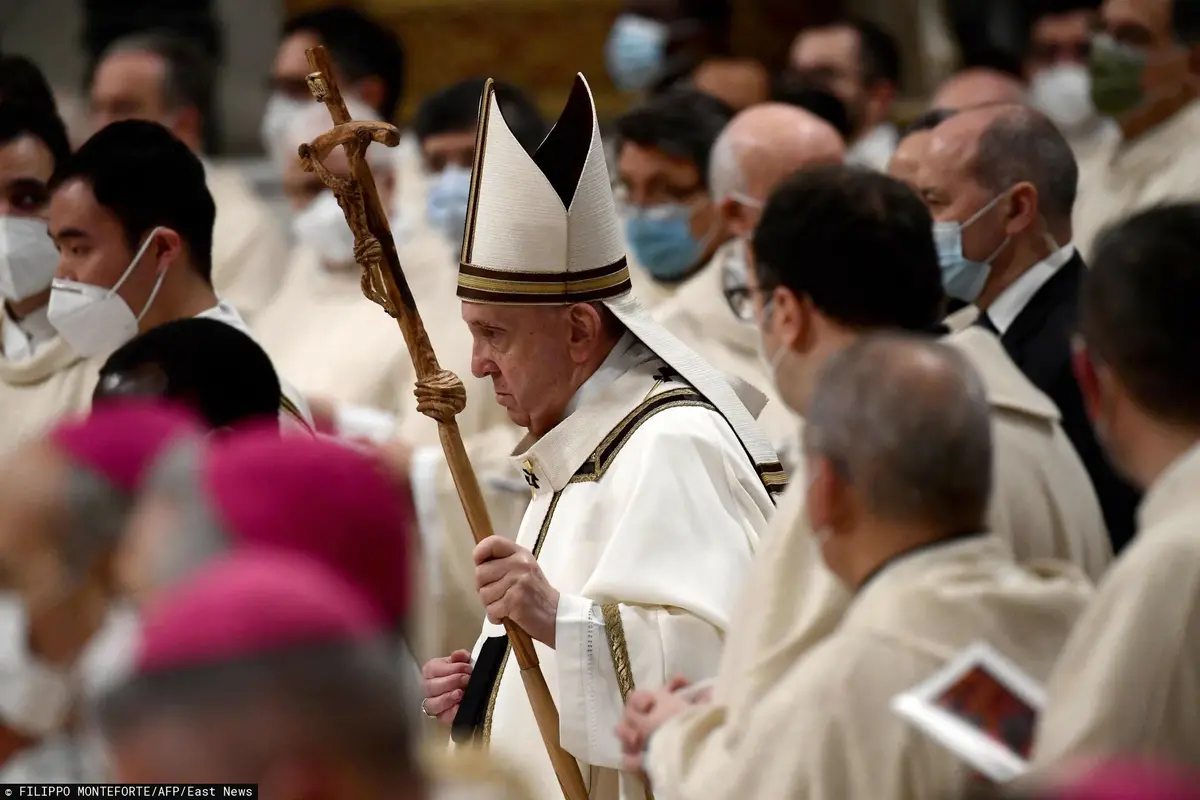 Papież Franciszek w czapce niesie krzyż.