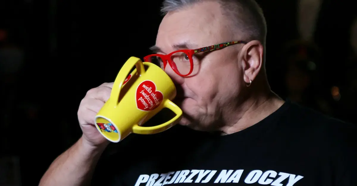 Jerzy Owsiak pije coś z kubka z logo WOŚP
