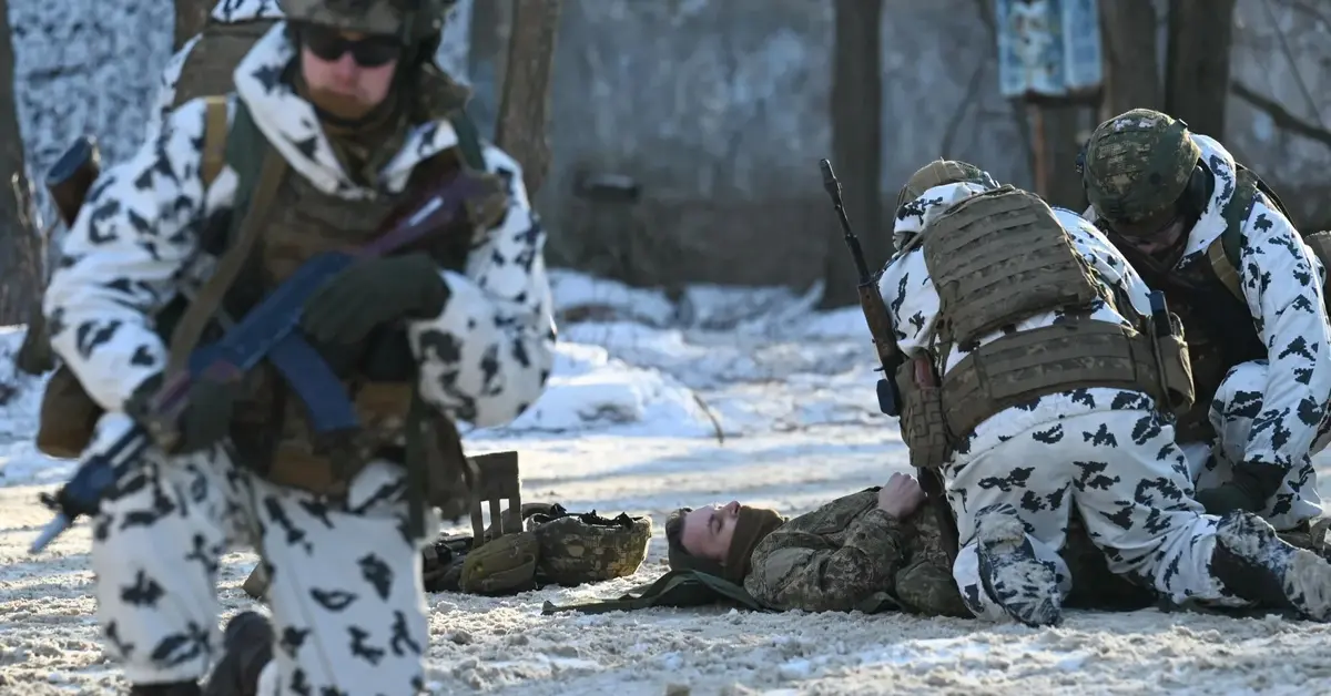 Rosyjscy żołnierze w białych kombinezonach udzielają pomocy rannemu leżącemu na ziemi