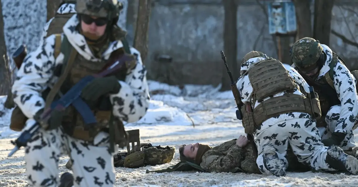 Rosyjscy żołnierze w białych kombinezonach udzielają pomocy rannemu leżącemu na ziemi