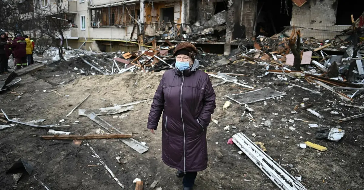 kobieta stojąca na tle bloku zniszczonego po ataku rosjan