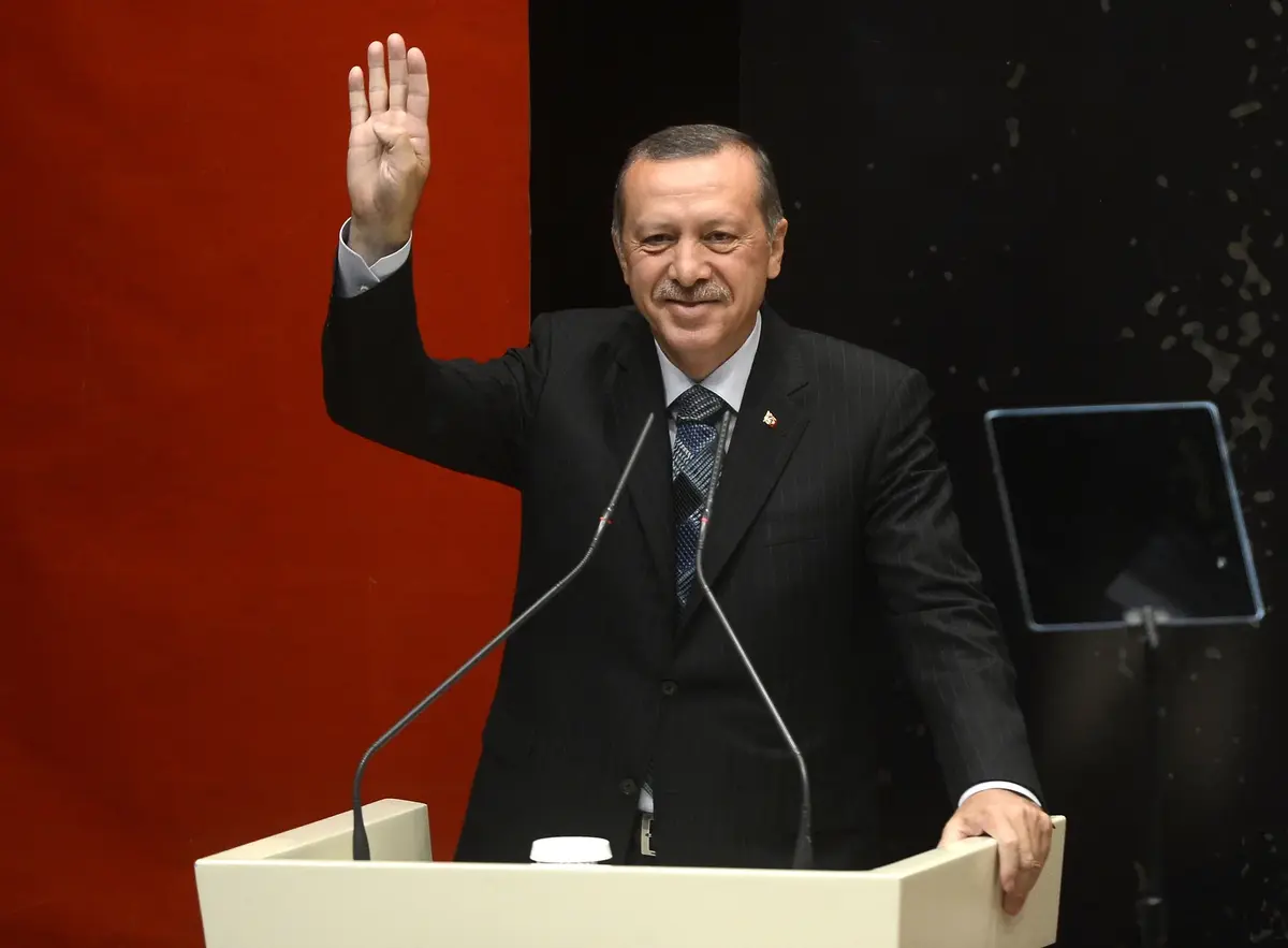 erdogan na mównicy z uśmiechem podnosi prawą rękę do góry 