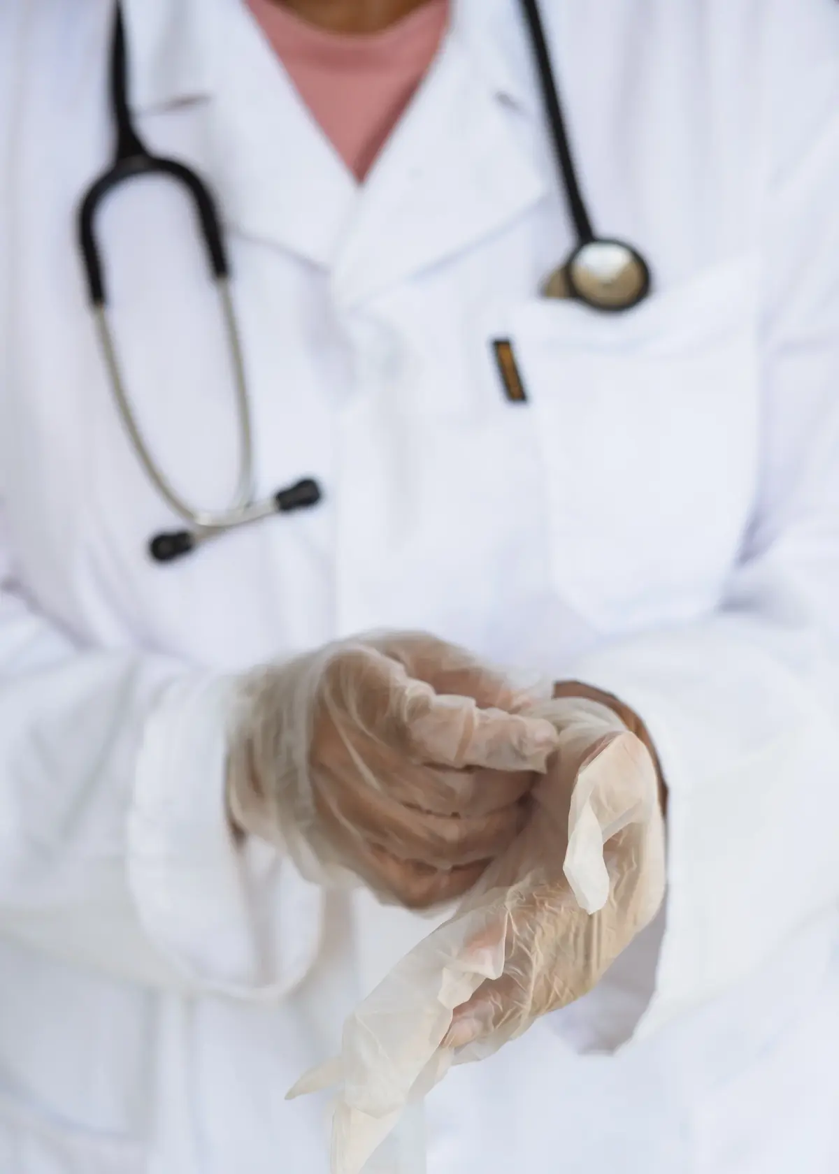 Lekarz w białym kitlu, ubiera foliowe rękawiczki na dłonie