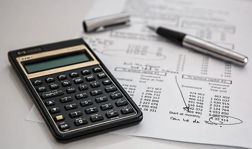 Kartka z wyliczeniami podatkowymi oraz kalkulator i długopis, leżące na białym stole