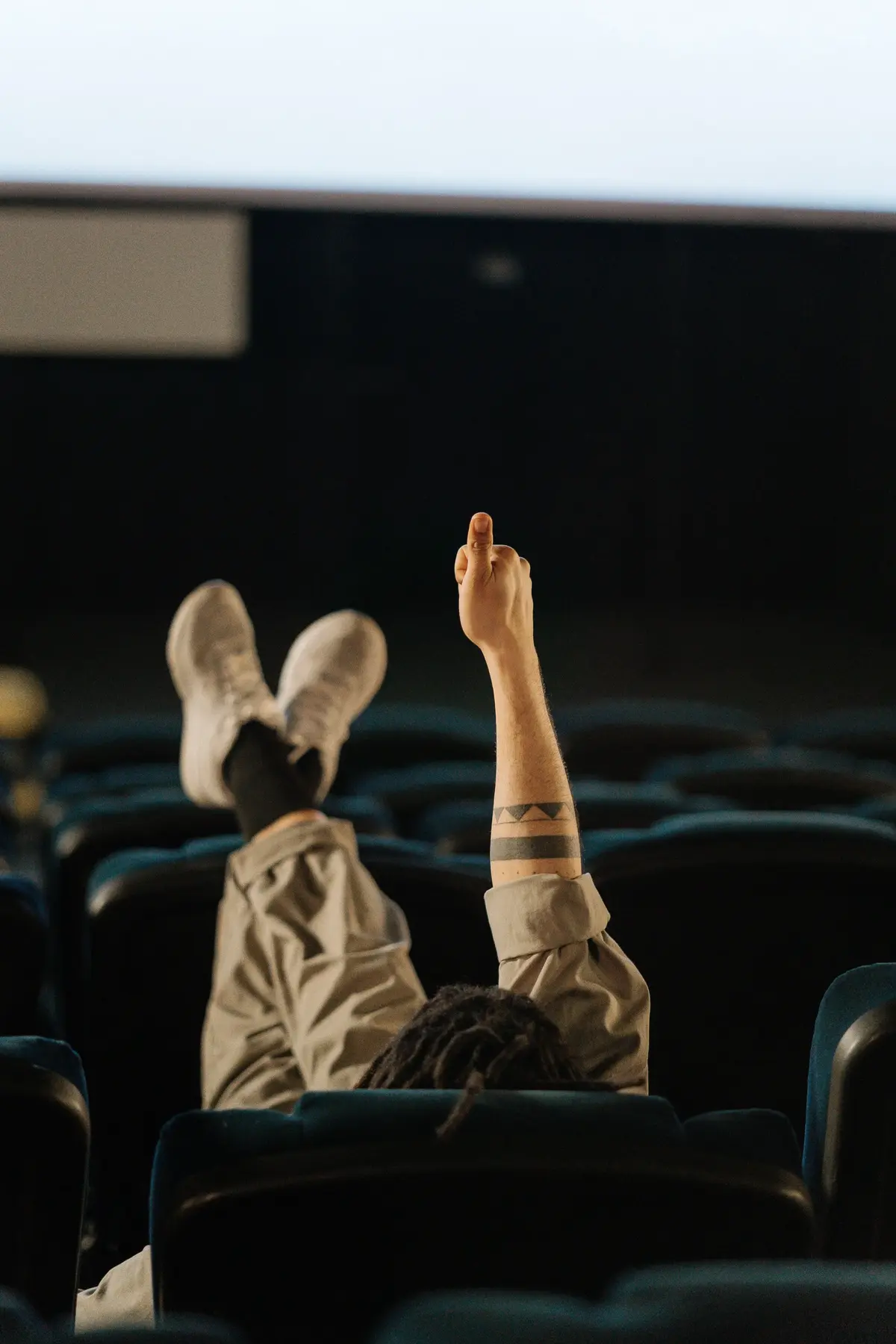 Mężczyzna siedzi w kinie, trzyma nogi na oparciu poprzedzającego siedzenia