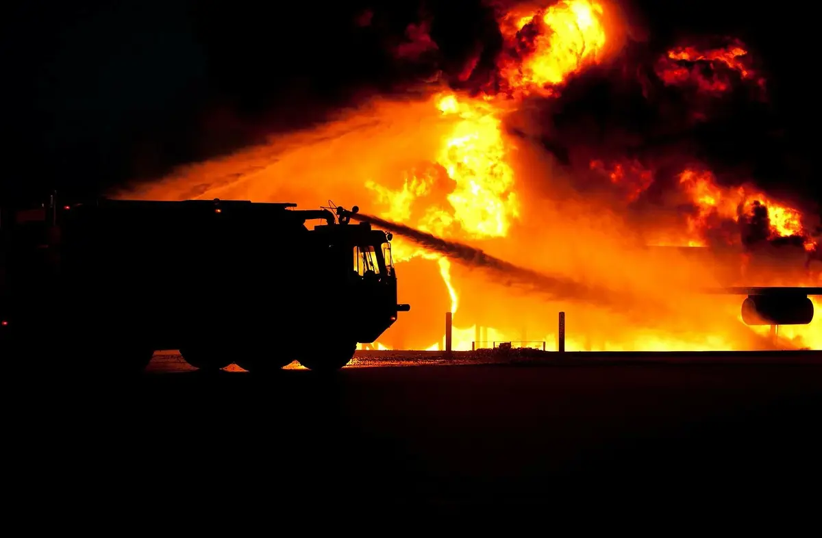 wóz gaśniczy gasi buchające w tle płomienie 