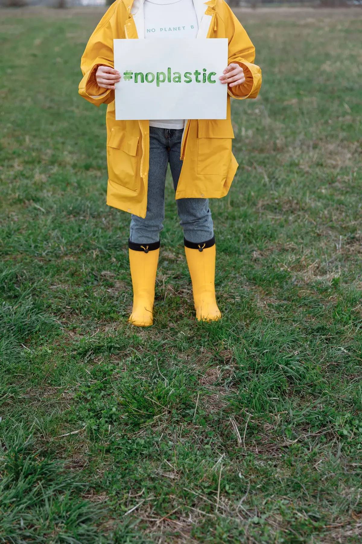 Osoba w żółtym płaszczu i kaloszach trzyma kartkę z napisem #noplastic