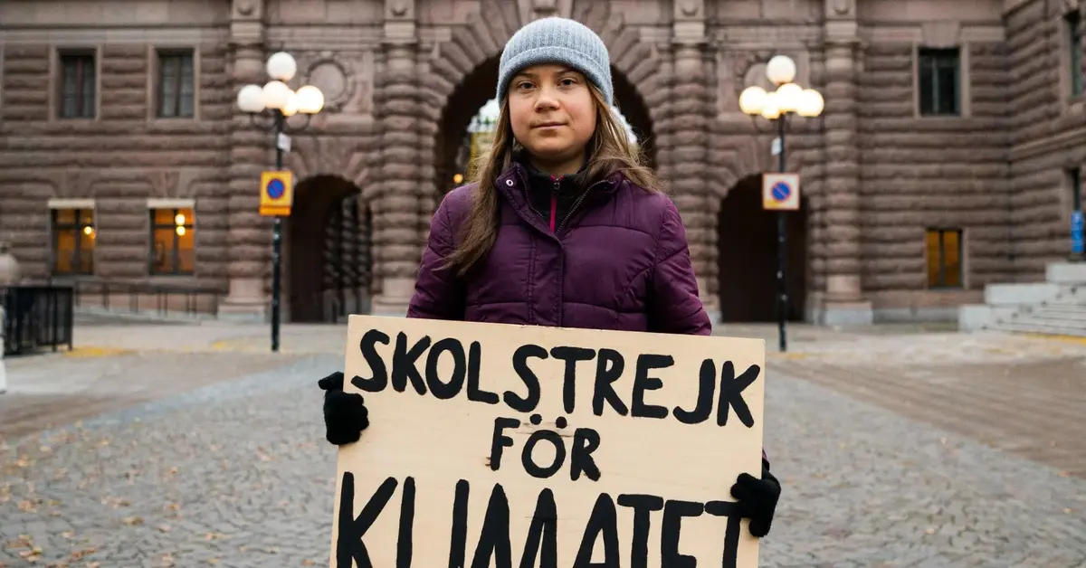 Greta Thunberg stoi trzymając plakat o tematyce ekologicznej