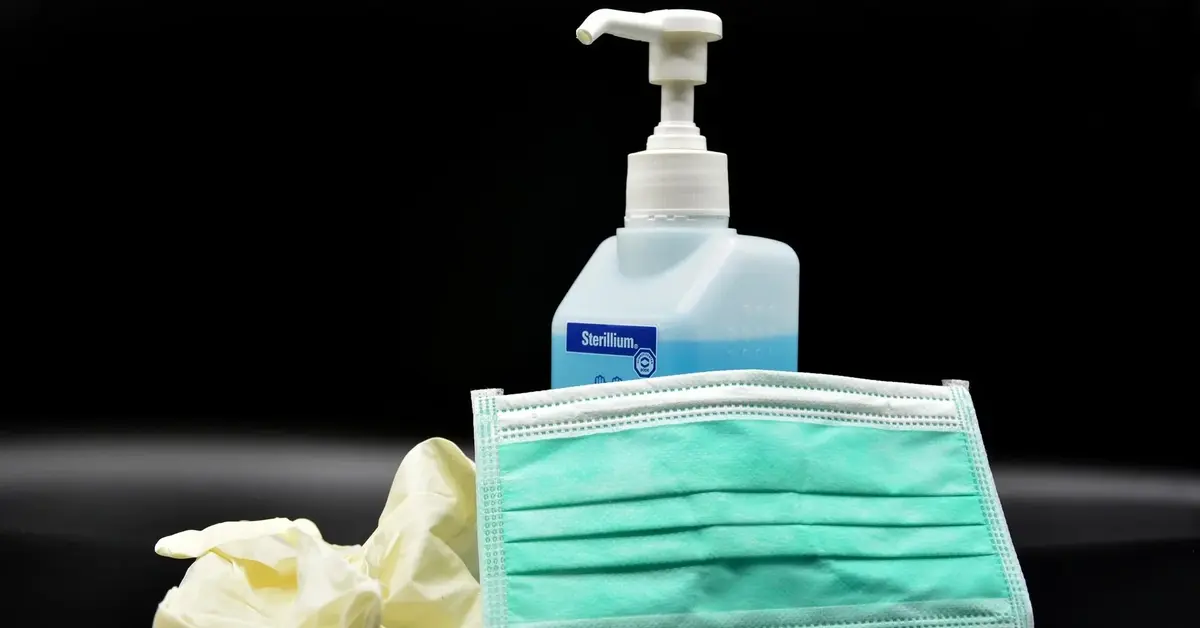 maseczka oraz rękawiczki obok pojemnika na płyn do dezynfekcji