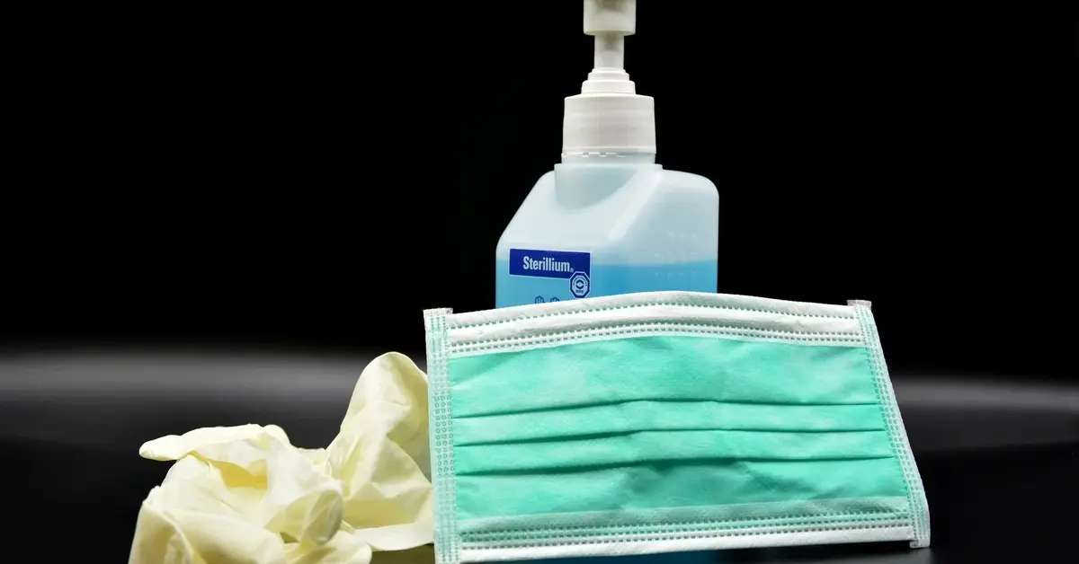 maseczka oraz rękawiczki obok pojemnika na płyn do dezynfekcji