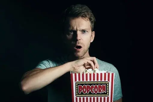 Mężczyzna z zaskoczoną miną je popcorn