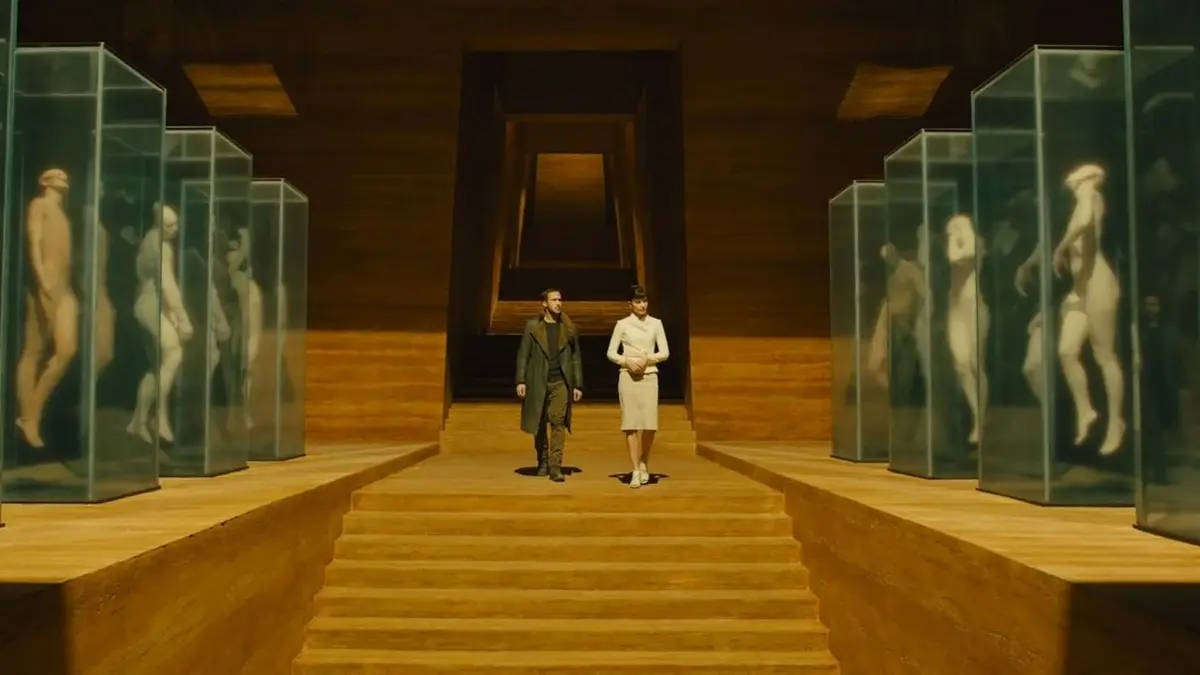 "Łowca androidów 2049" - Ryan Gosling idzie środkiem żółtej sali z androidami w gablotach