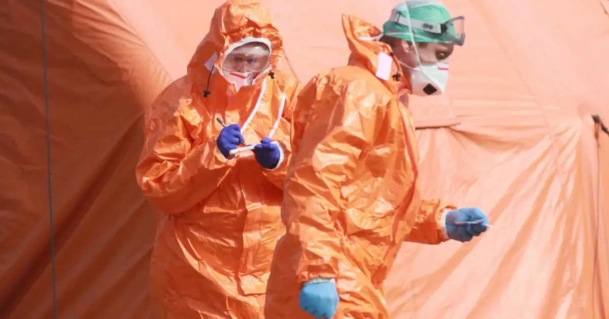 Mężczyźni ubrani w pomarańczowe kombinezony, chroniące ich przed zakażeniem koronawirusa