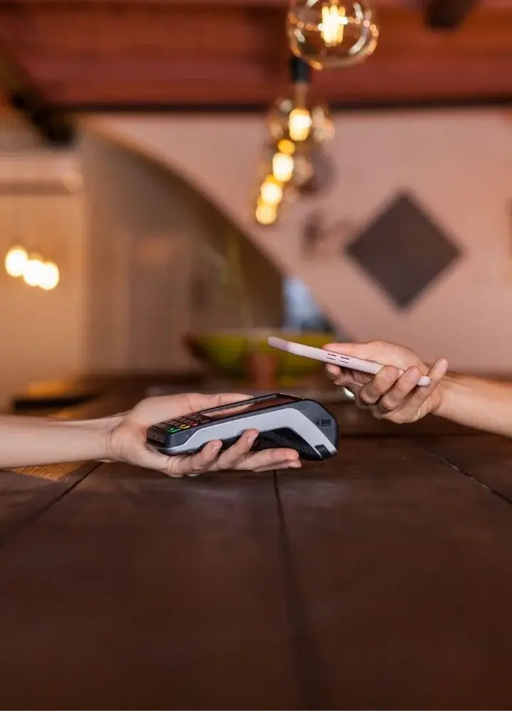 Dłoń trzymająca telefon nad dłonią trzymającą terminal płatniczy na tle restauracji