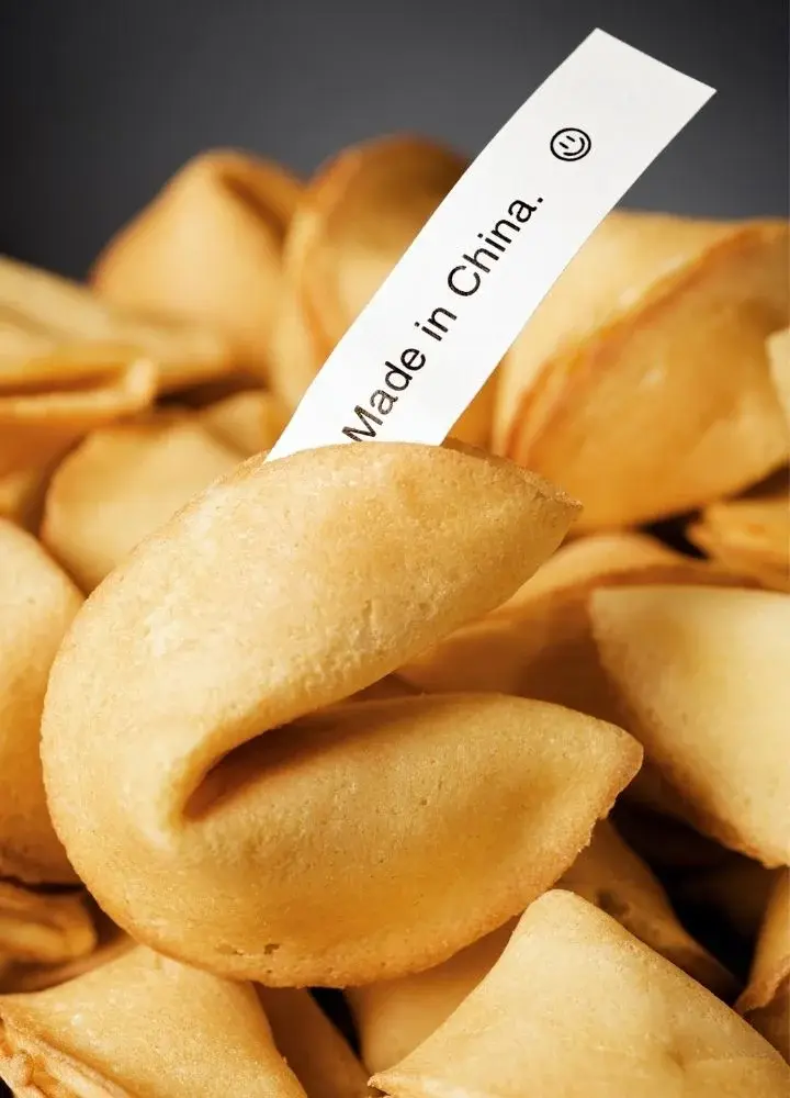 Ciasteczko na tle pozostałych chińskich ciastek z wróżbą z białą, podłużną karteczką z napisem "Made in China"