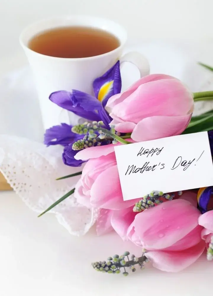 Bukiet różowych tulipanów z małą, prostokątną karteczką z napisem "Happy Mother's Day" na stole na tle filiżanki z kawą