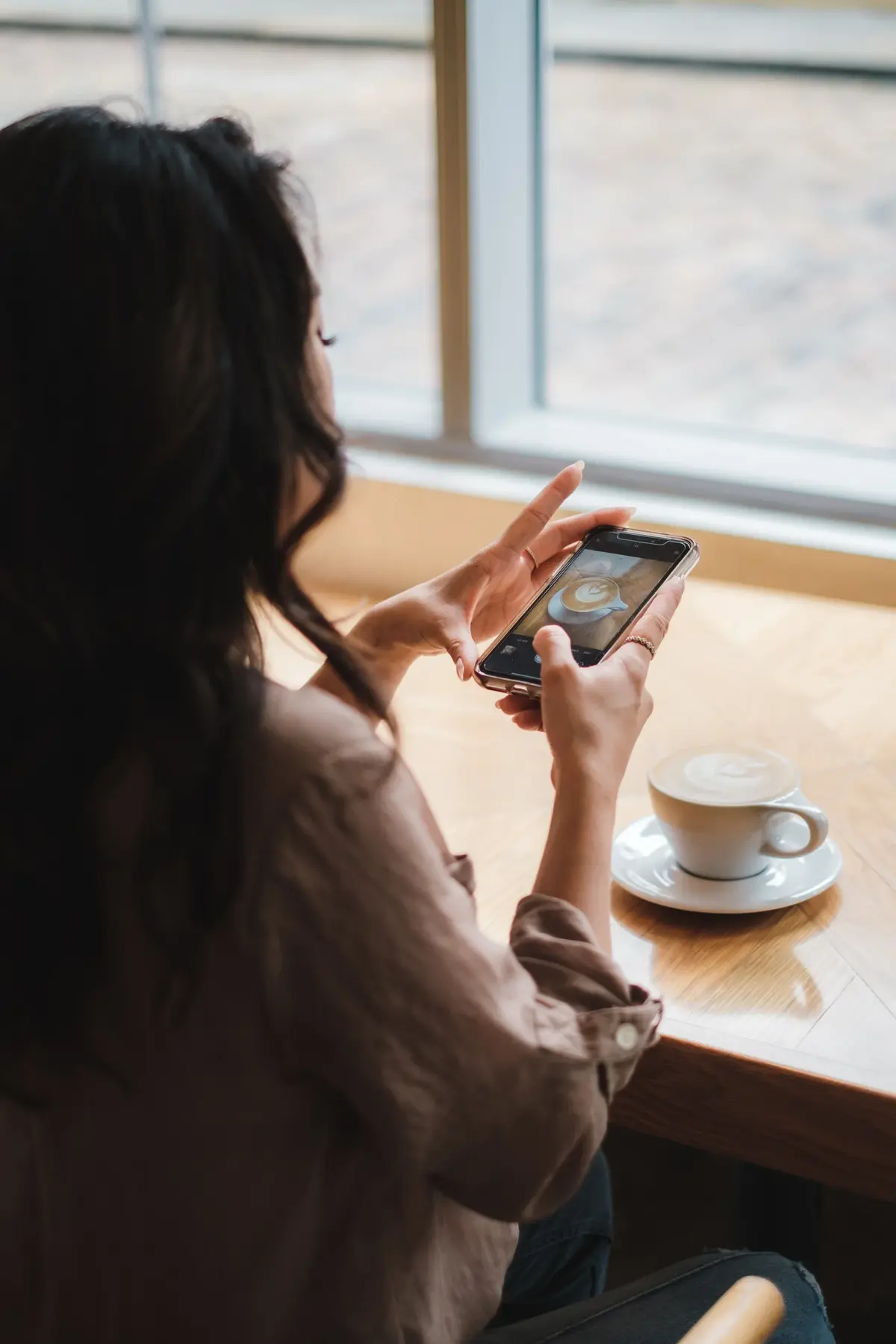 Kobieta siedzi w kawiarni z telefonem w dłoni i robi zdjęcie kawy