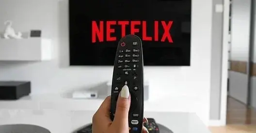Mężczyzna trzyma w dłoni pilota, a na telewizorze otwiera się aplikacja Netflix