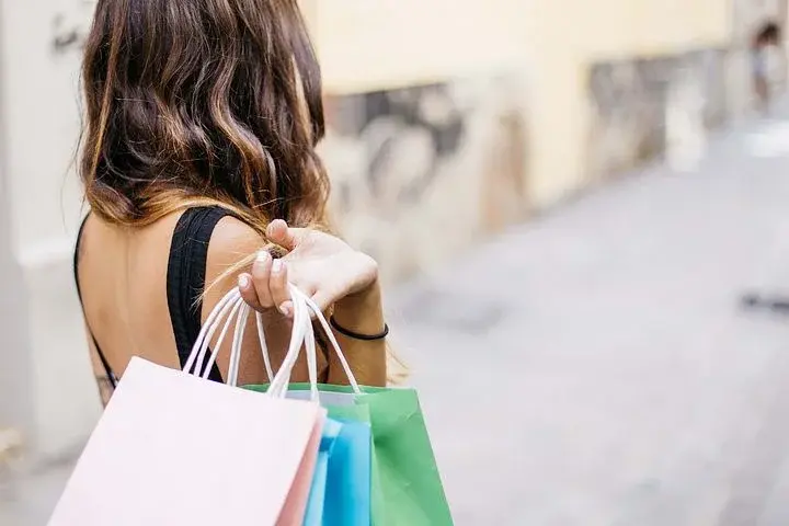 Kobieta trzyma w prawej dłoni kolorowe papierowe torby na zakupy