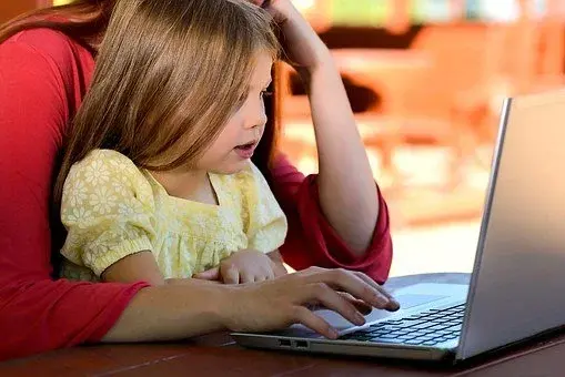 Kobieta siedzi z dziewczynką na kolanach i obie przeglądają strony internetowe na laptopie