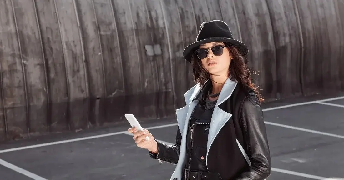 Kobieta w kapeluszu i okularów z telefonem w ręku na ulicy