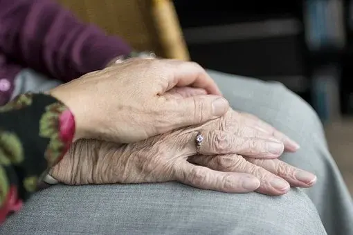 Ręce starszej kobiety na kolanach, dotykane przez rękę młodszej osoby