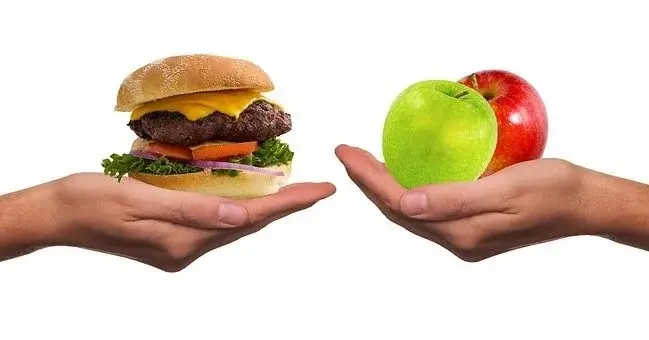 Grafika przedsaiwjaąca dwie dłonie - jedna osoba trzyma hamburgera mięsnego, a druga jabłka