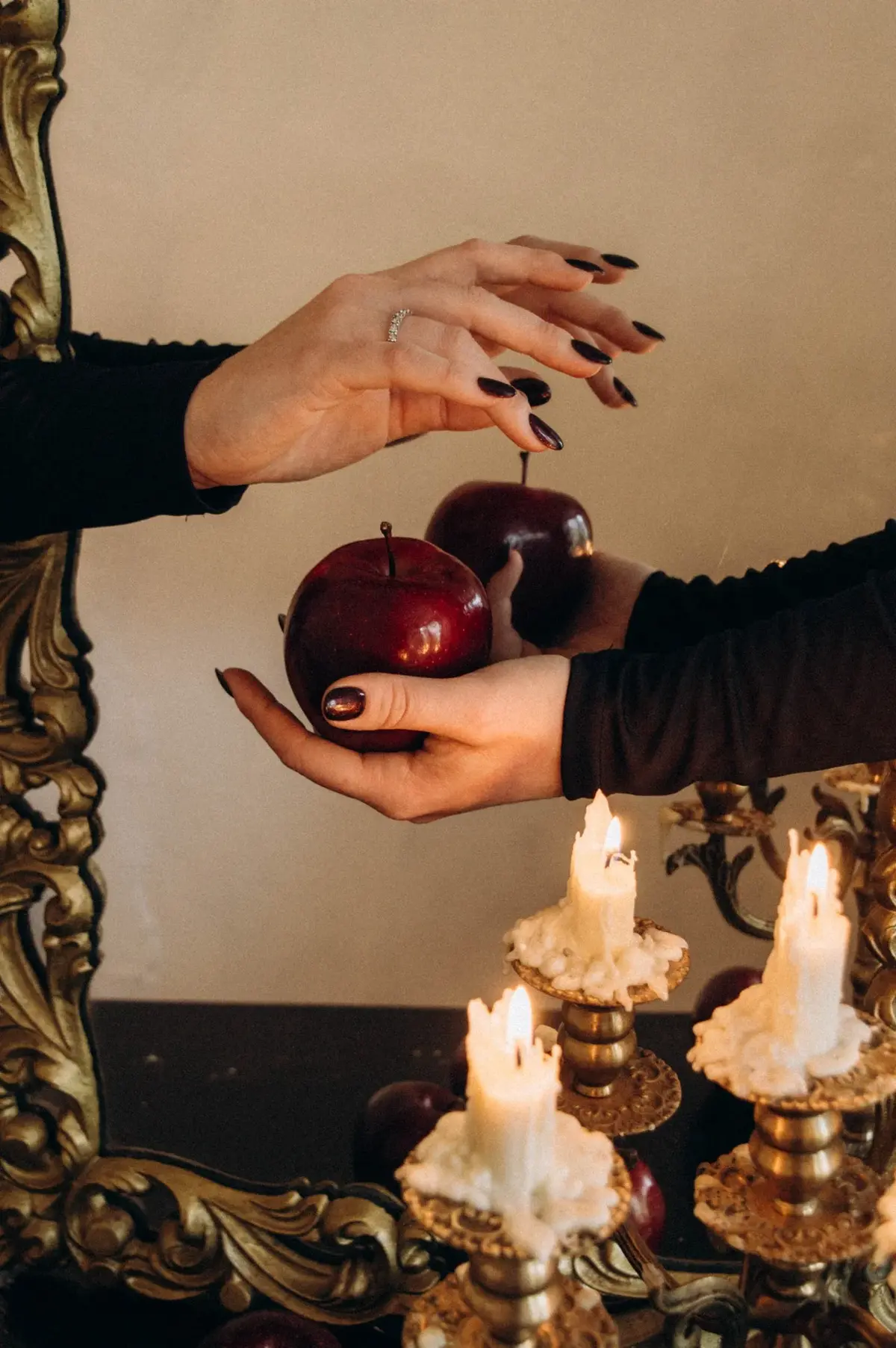 Kobiece dłonie trzymające w garści bordowe jabłka na tle kobiecych dłoni i świeczek