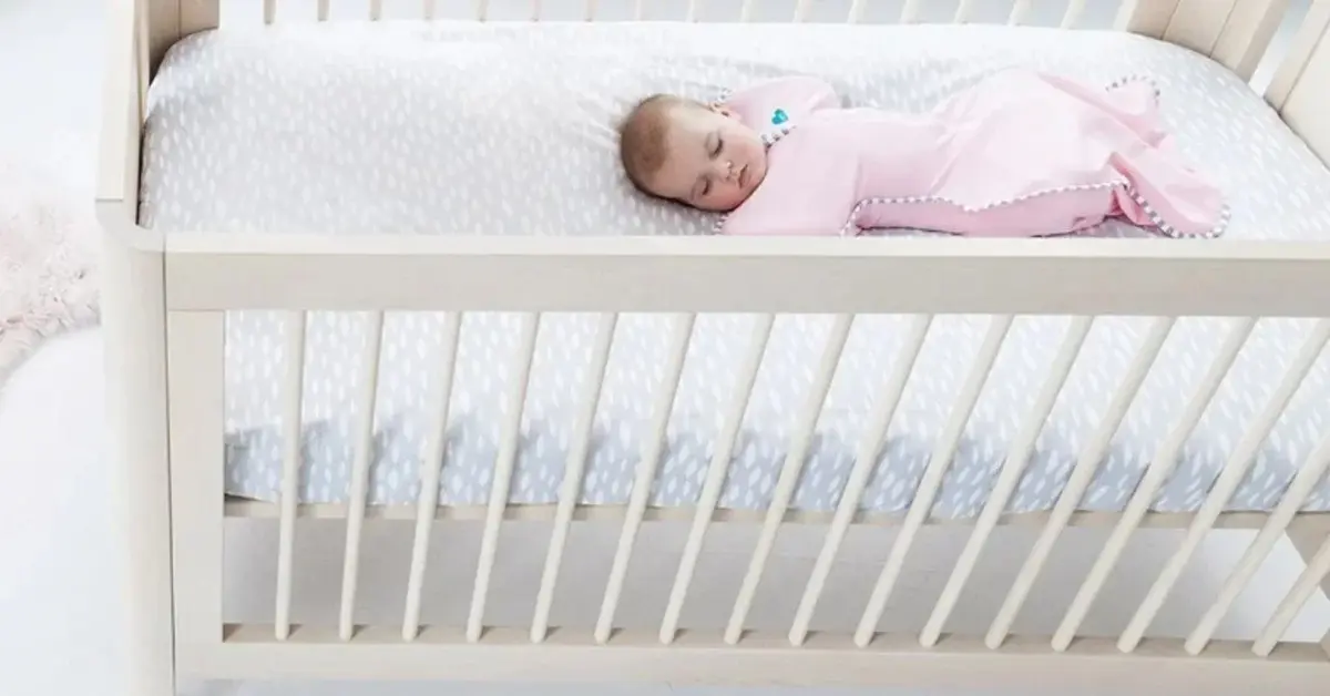 Dziecko w otulaczu różowym w łóżeczku ze szczebelkami